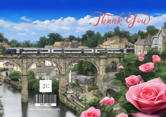 A train passes over a stone bridge with a river below, surrounded by flowers and trees.