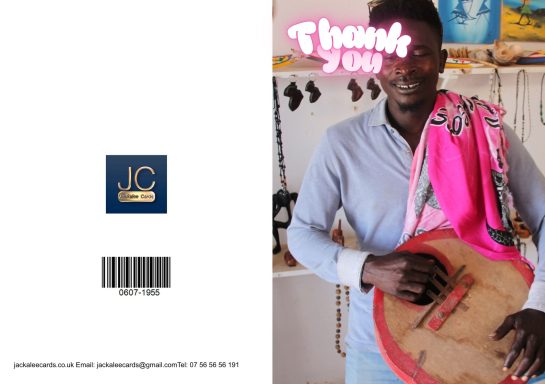 A man stands holding a traditional musical instrument, smiling in a vibrant market setting.