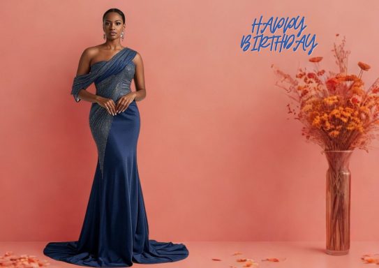 JC 007 Woman in a navy blue gown standing against a pink backdrop, with flowers nearby.